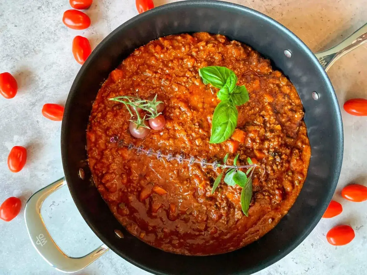 Herzhafte rotwein bolognese in einer Pfanne, garniert mit frischem Basilikum und Kirschtomaten.
