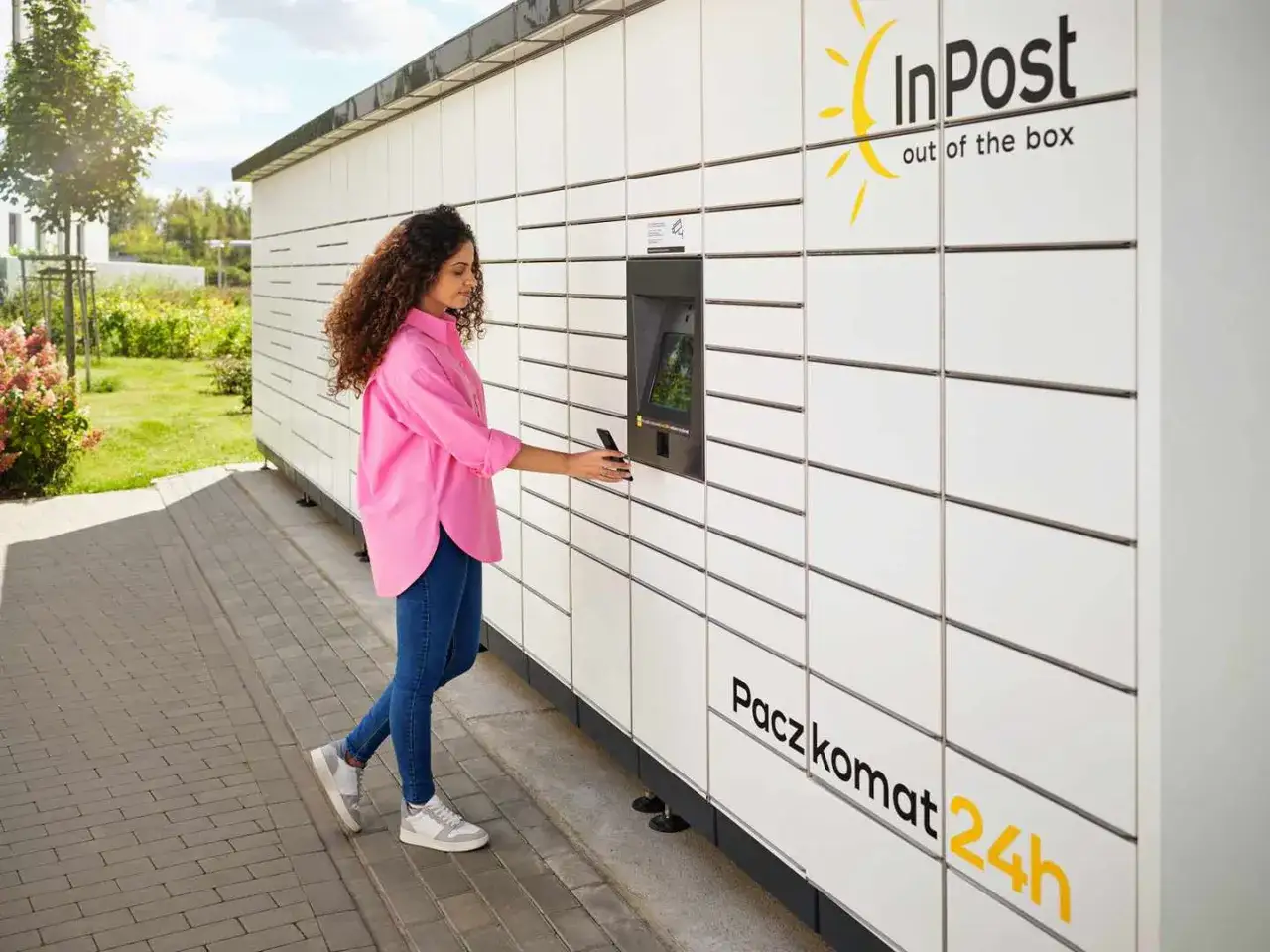 Kobieta z telefonem przy Paczkomacie InPost. To wygodne miejsce nadania przesyłek.