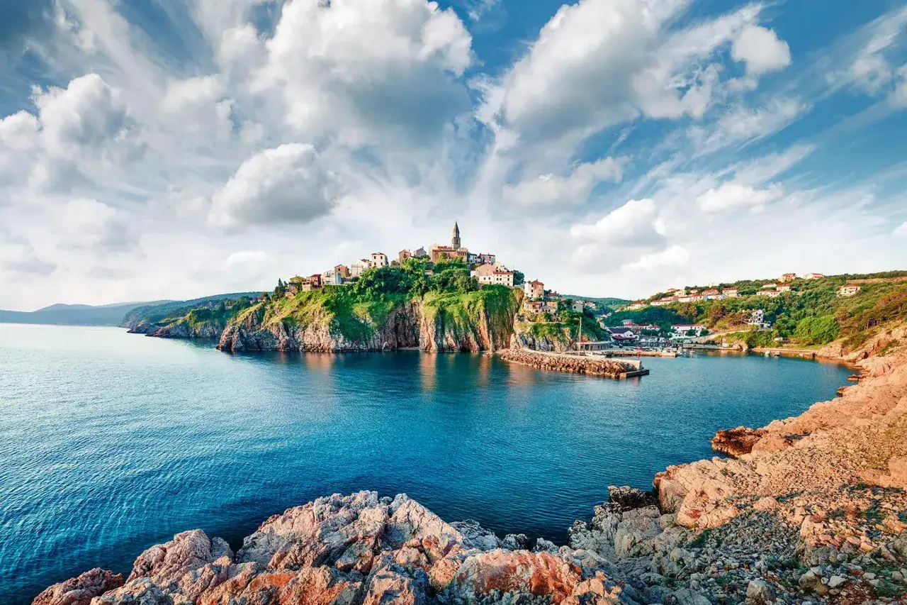Malowniczy port w Chorwacji, z miasteczkiem na wzgórzu i turkusową wodą.