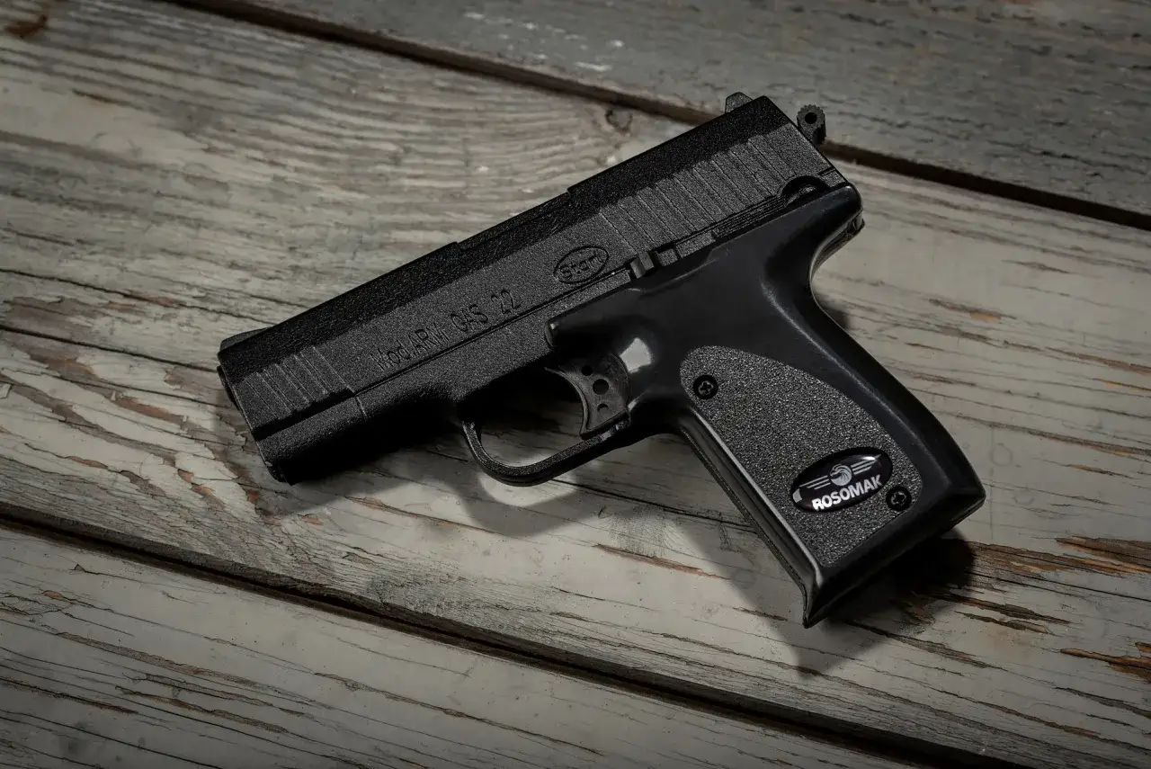 Czarny pistolet gazowy na drewnianym blacie. Symbolizuje potencjalne naruszenie miru domowego, budząc niepok&oacute;j.
