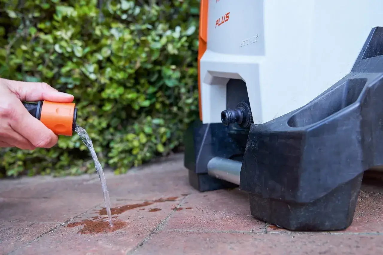 Mano conecta manguera a hidrolimpiadora para su mantenimiento. Agua fluye sobre el suelo.