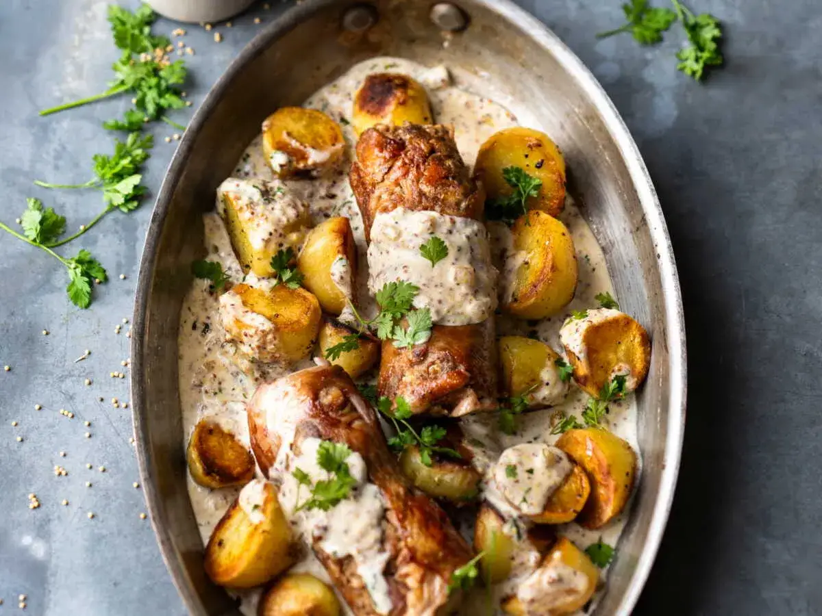 Une délicieuse saucisse andouillette coupée en tronçons, servie avec des pommes de terre rôties et une sauce crémeuse à la moutarde, le tout garni de persil frais.