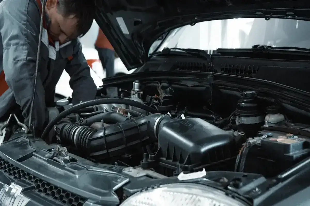 Mechanik naprawia silnik, gdy auto traci moc. Widać elementy układu dolotowego i akumulator.