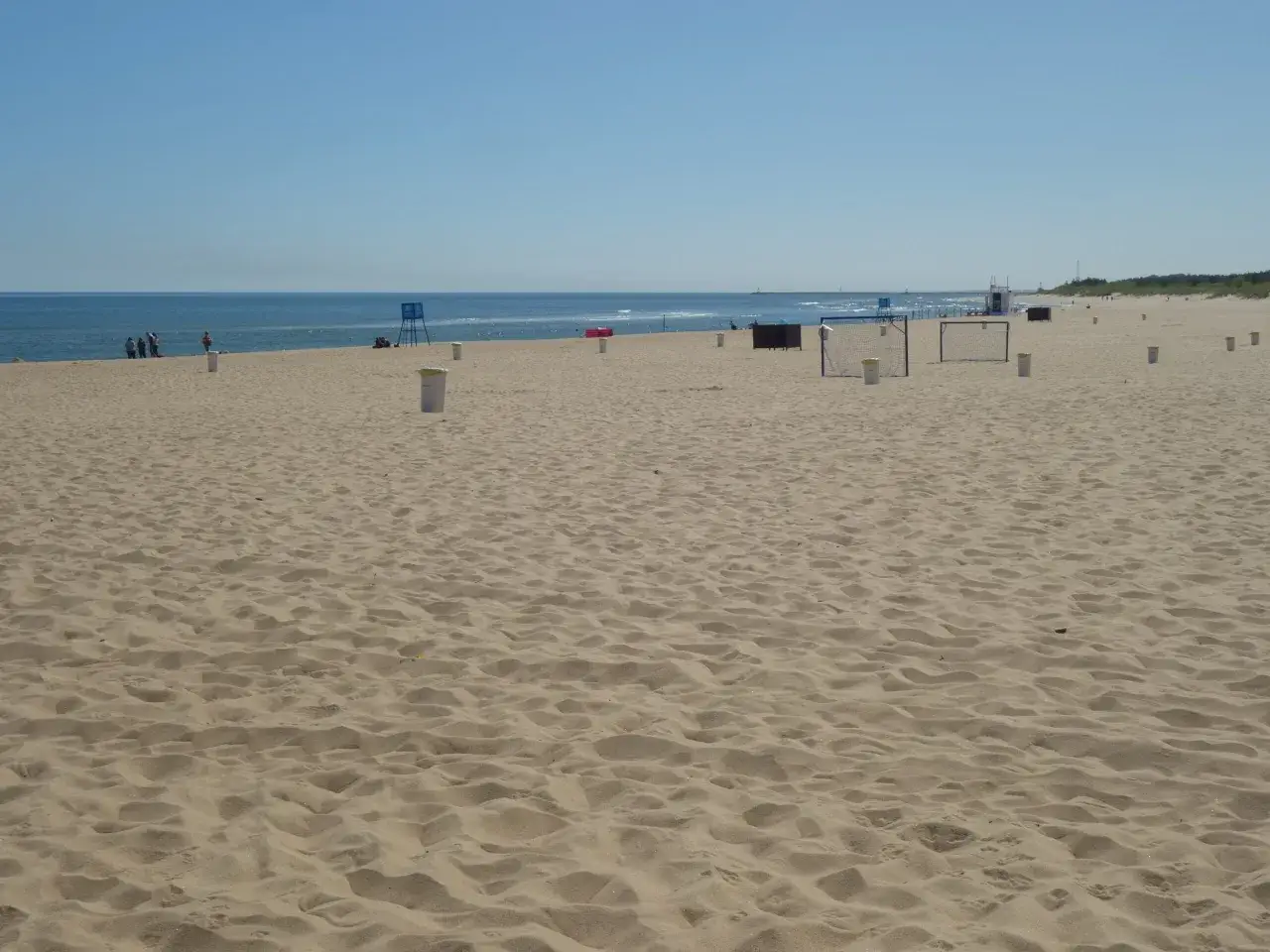 Piękna plaża w Gdańsku, idealne miejsce, gdzie na spacer. W tle widać morze i niebo, a na piasku kosze na śmieci i bramki do gry.