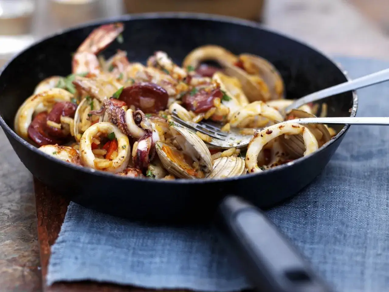 Eine köstliche Paella mit Garnelen, Tintenfischringen, Muscheln und Chorizo in einer Pfanne.