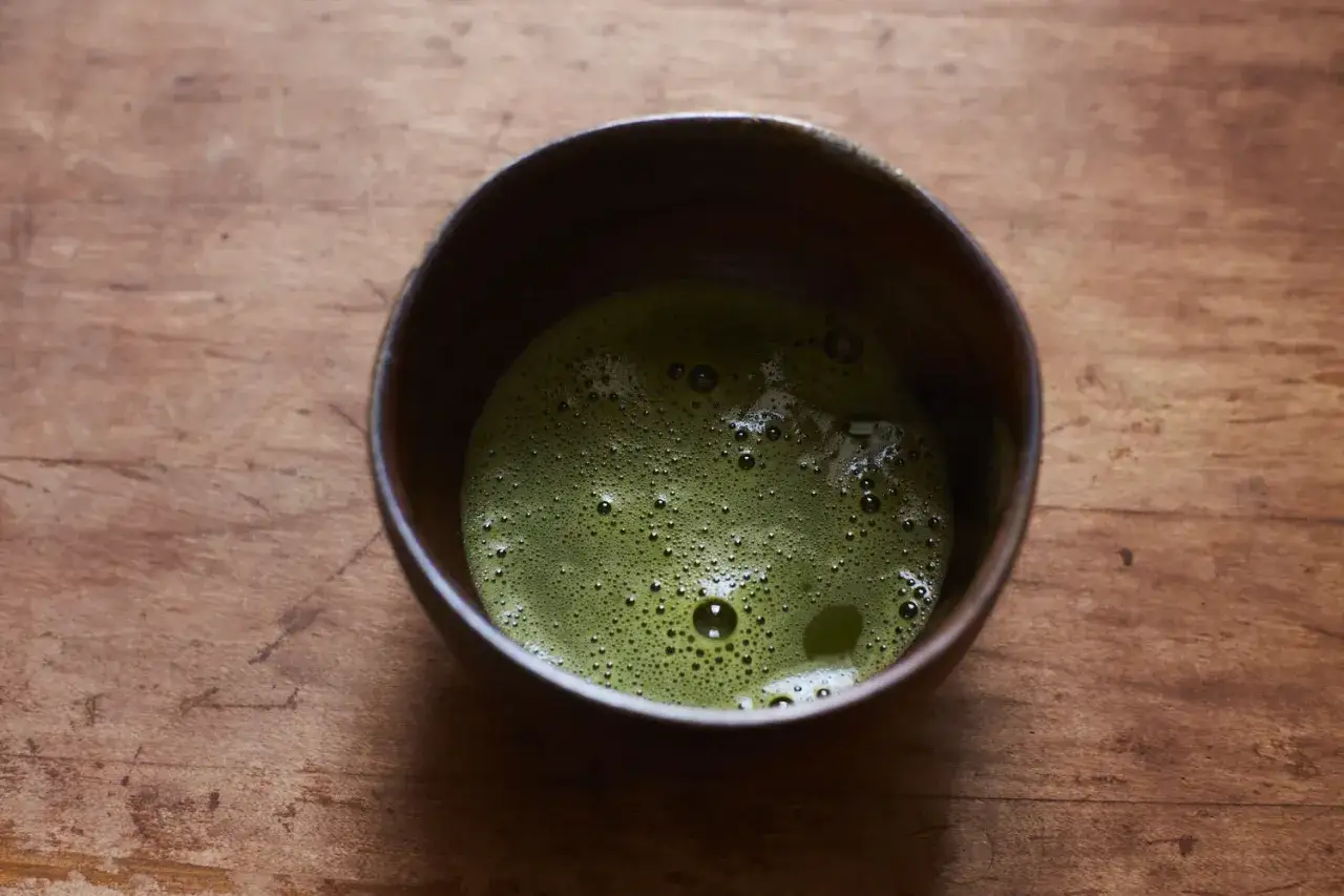 Zielona, spieniona matcha w ceramicznej miseczce na drewnianym tle. To właśnie matcha, tradycyjny japoński napój.