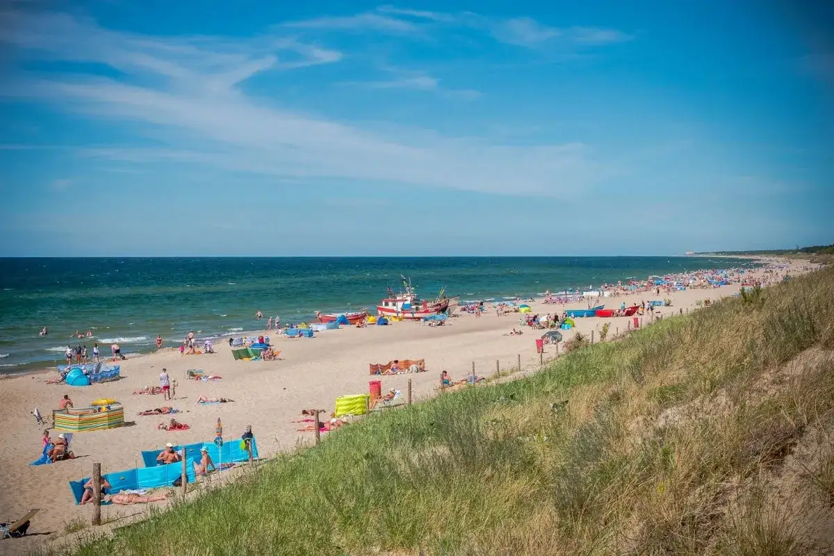 Słoneczna plaża w Dąbkach pełna turyst&oacute;w, kolorowych parawan&oacute;w i łodzi. Idealne miejsce na wakacyjne atrakcje nad Bałtykiem.
