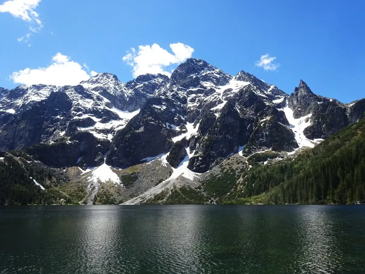 Jezioro Morskie Oko u stóp Rysów, najwyższego szczytu w Polsce, w otoczeniu skalistych gór i zielonych lasów.