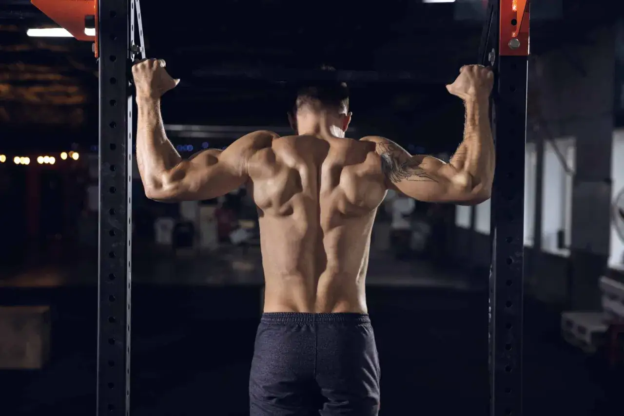 Muskul&ouml;s man g&ouml;r pull ups i ett gym.