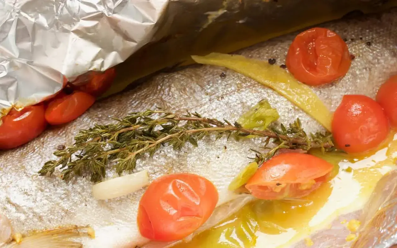 Frische Forelle vom Grill in Alufolie mit Tomaten, Zitrone und Kräutern.