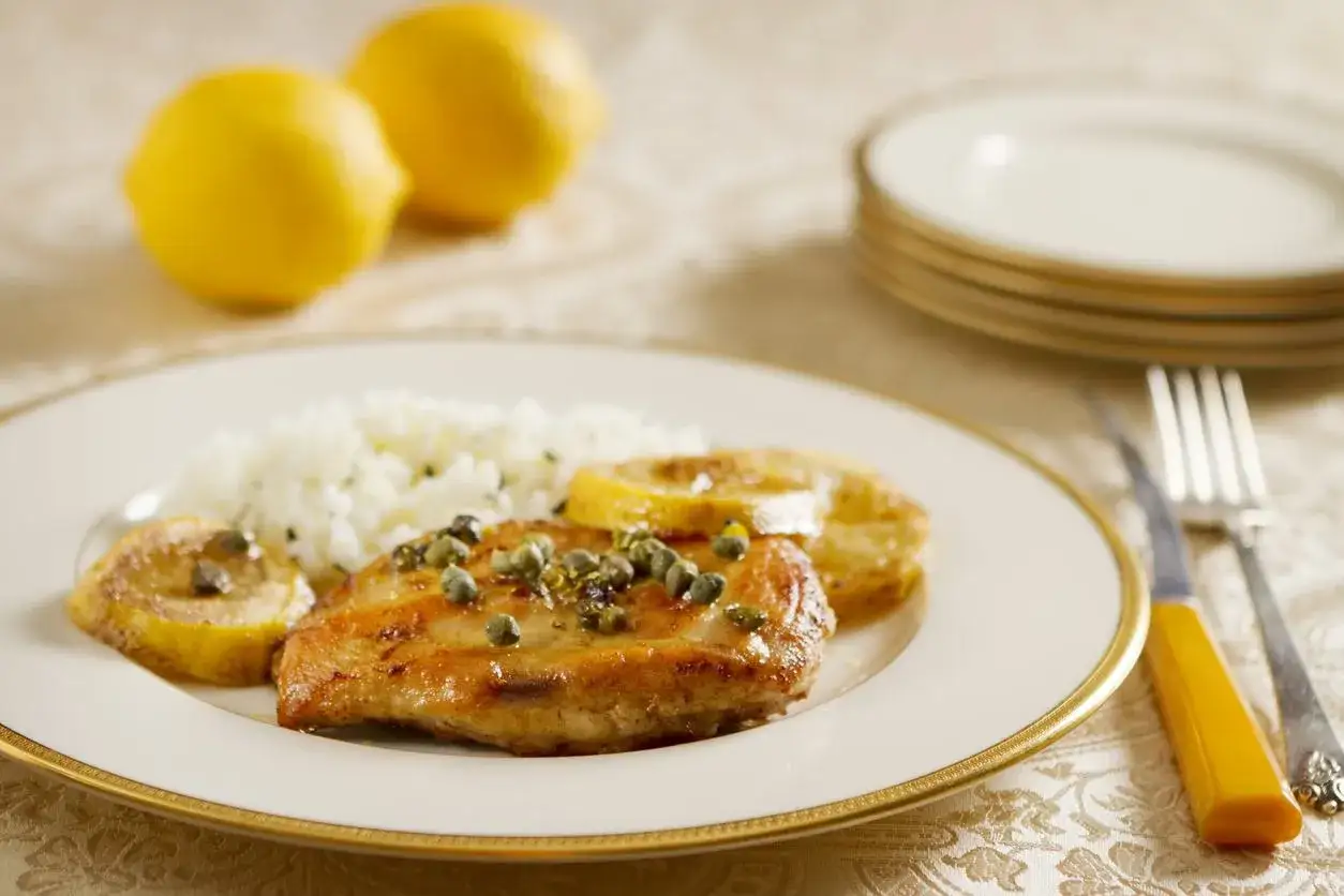 En tallrik med kyckling piccata, ris och citronklyftor.