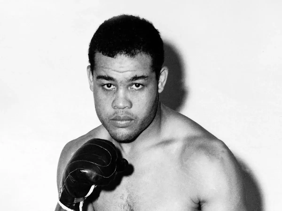 Joe Louis, a legendary boxer, poses with a boxing glove, hinting at his rigorous training routine.