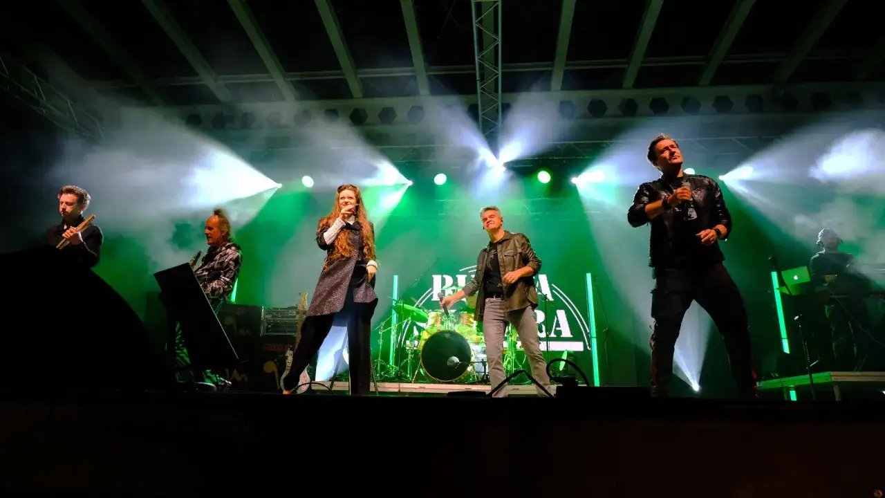 Zespół Budka Suflera na scenie, w zielonych światłach i dymie. Wokalistka śpiewa, gitarzyści grają, a perkusja czeka na swój moment.
