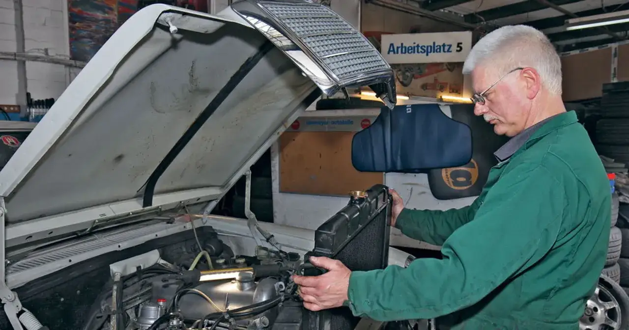 Mechanik w zielonym kombinezonie wykonuje wymianę chłodnicy w samochodzie.