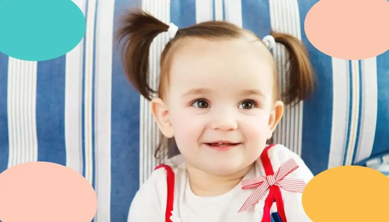 Un tierno sue&ntilde;o de beb&eacute; de 19 meses, con coletas y una sonrisa contagiosa, descansa sobre un sof&aacute; de rayas azules.