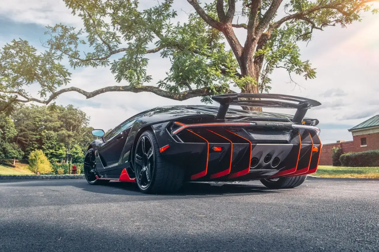 Czarny Lamborghini Centenario z pomarańczowymi akcentami stoi pod drzewem.