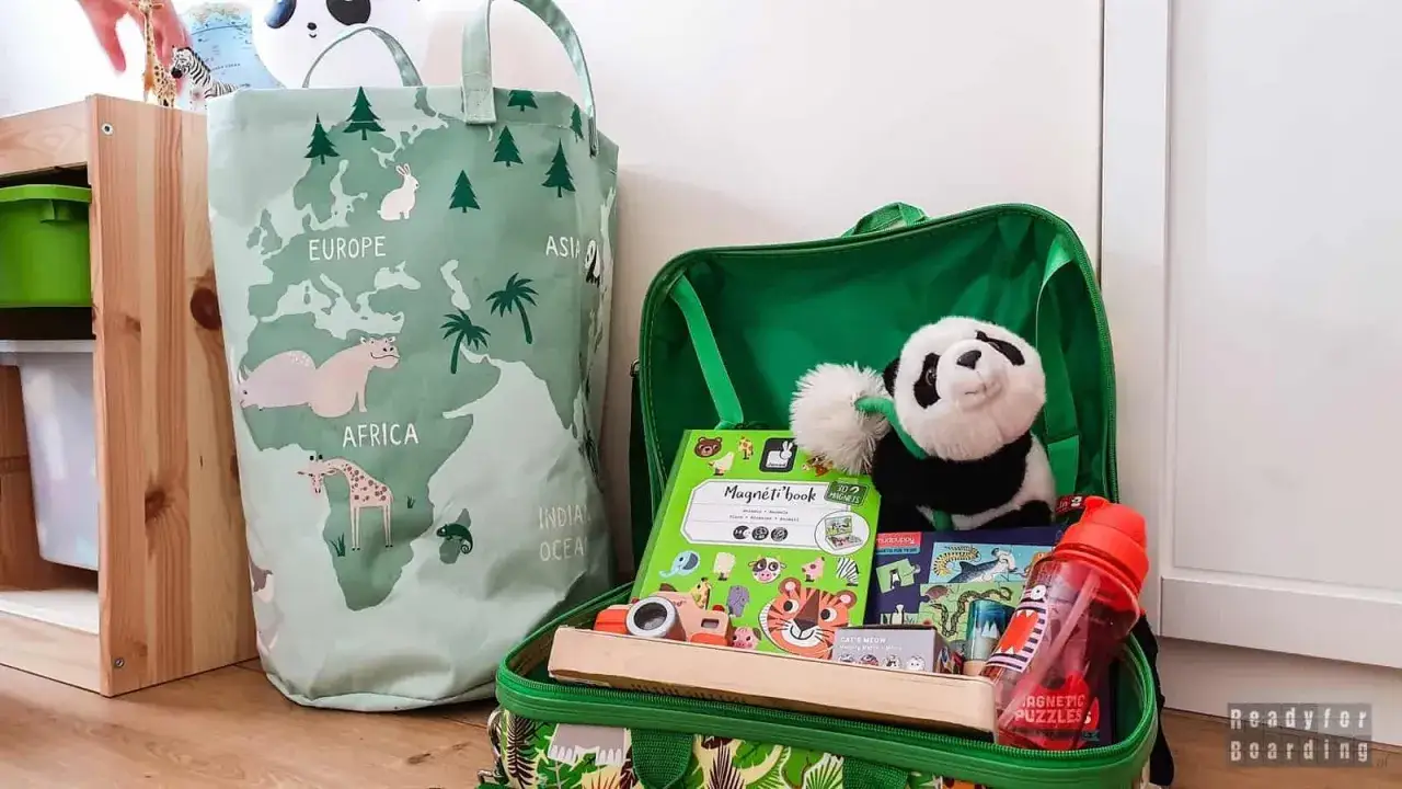 Zielona torba z mapą świata i plecak pełen zabawek, idealne na zabawy w aucie. Pluszowa panda, książeczki i drewniane zabawki czekają na podr&oacute;ż.