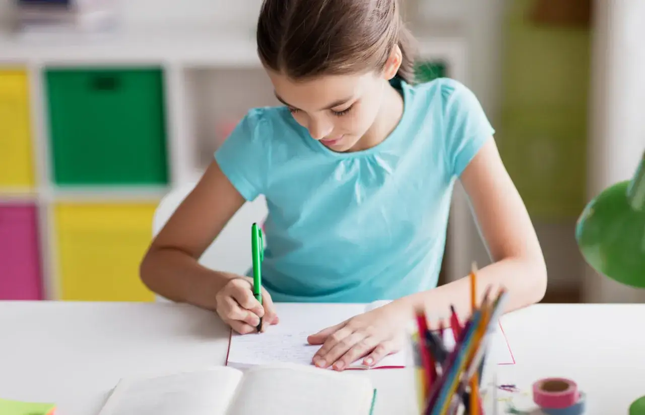 Ein Mädchen schreibt konzentriert in ein Heft. Sie lernt vielleicht gerade verschiedene Gedichtformen für die Grundschule.