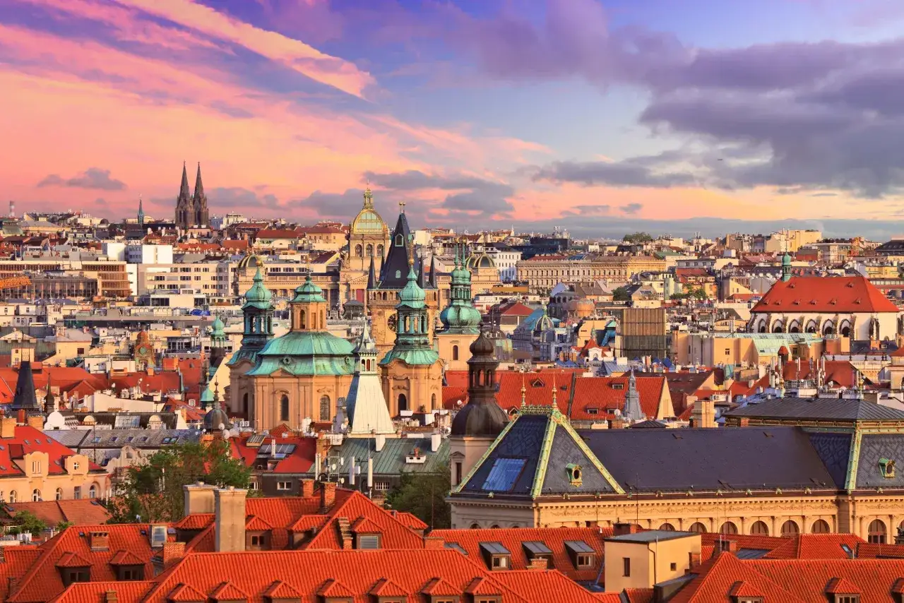 Vue panoramique de Prague au coucher du soleil, avec ses toits rouges et ses dômes verts. Une visite à Prague inoubliable.