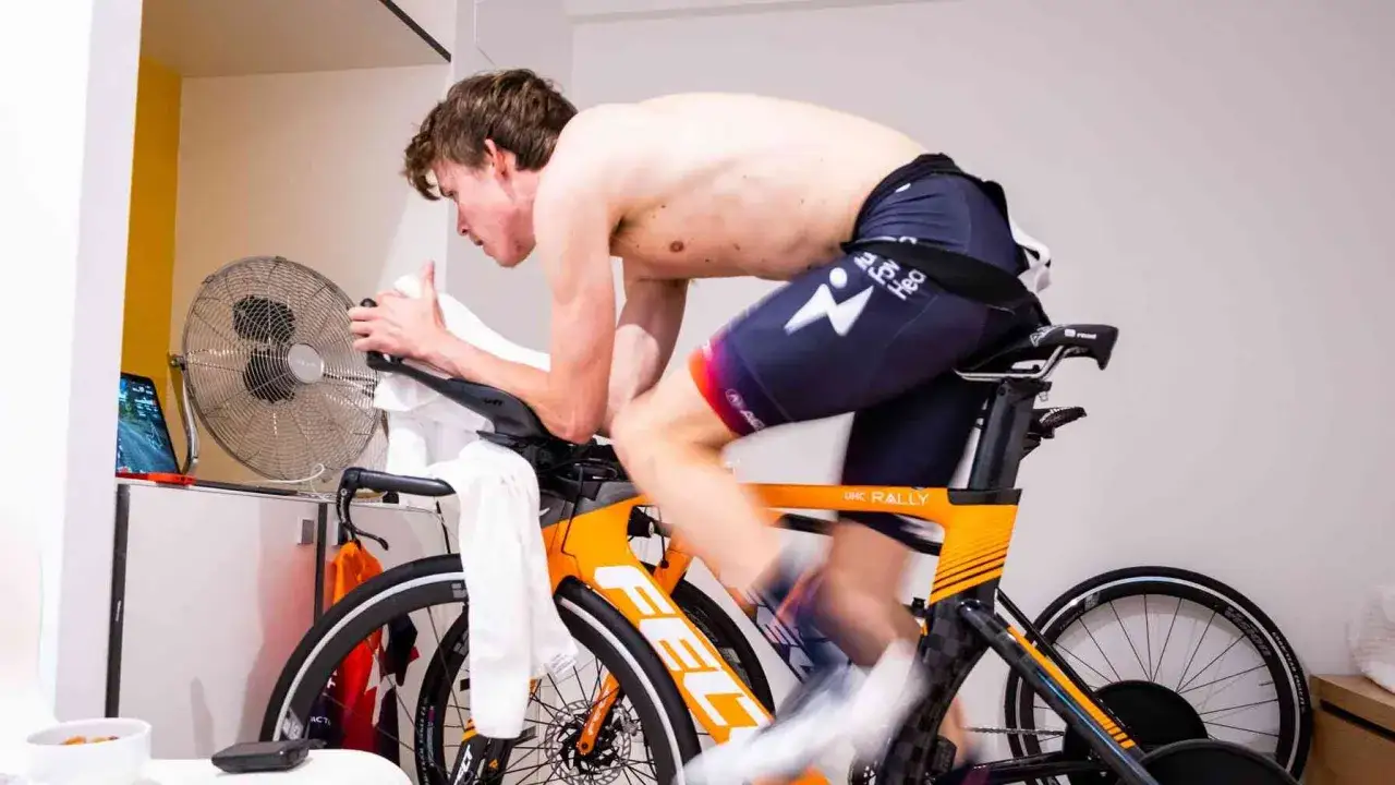 Wout van Aert trains intensely on his bike, a fan blowing to cool him. He's focused, pushing hard, but thankfully no crash in sight.