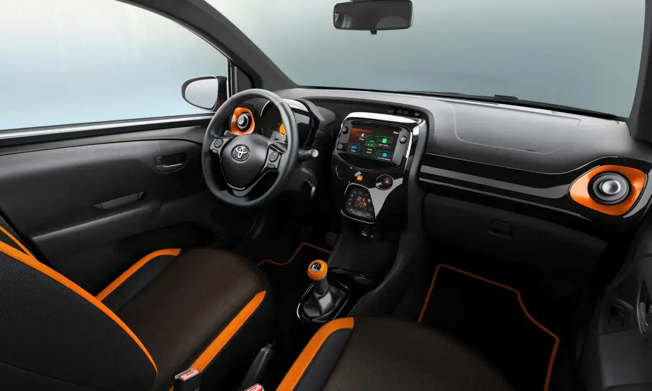 Wnętrze Toyoty Aygo 2020 z pomarańczowymi akcentami na siedzeniach, kierownicy i desce rozdzielczej.