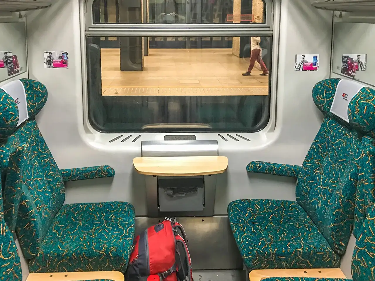 Innenansicht eines Zugabteils. Zwei Sitze mit t&uuml;rkisfarbenem Muster sind zu sehen. Ein Rucksack liegt auf dem Boden. Die Reise von Berlin nach Warschau beginnt.
