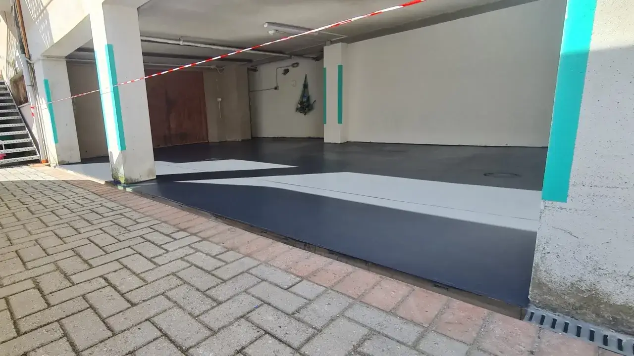 Pavimentazione garage in corso: il nuovo pavimento grigio scuro è pronto, con nastro di segnalazione rosso/bianco.