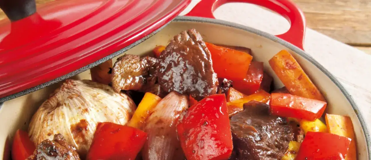 Fleisch mit Paprika und Knoblauch in einem roten Topf, bereit, um langsam zu schmoren.