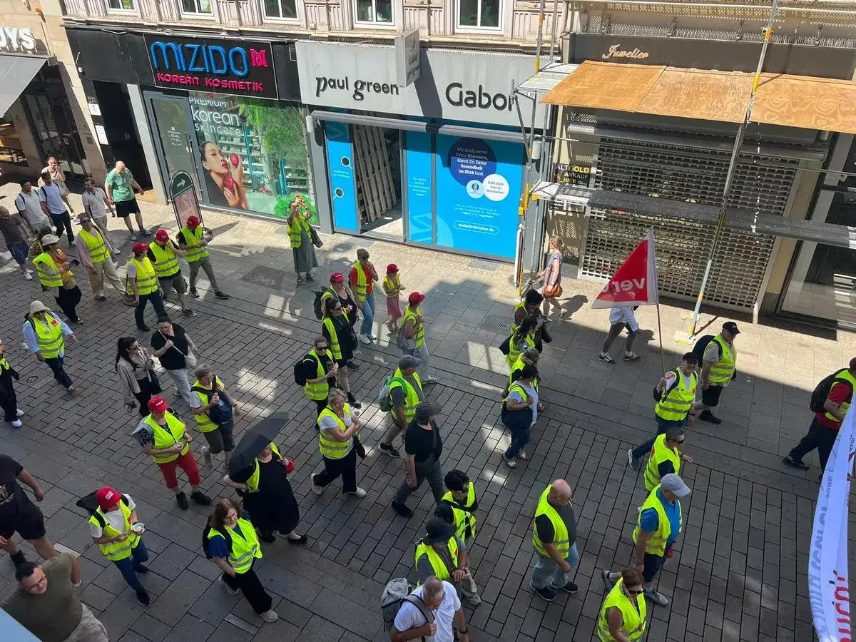 Menschen in Warnwesten marschieren auf einer Straße, einige tragen Fahnen. Ein **Streik im Handel** ist deutlich erkennbar.