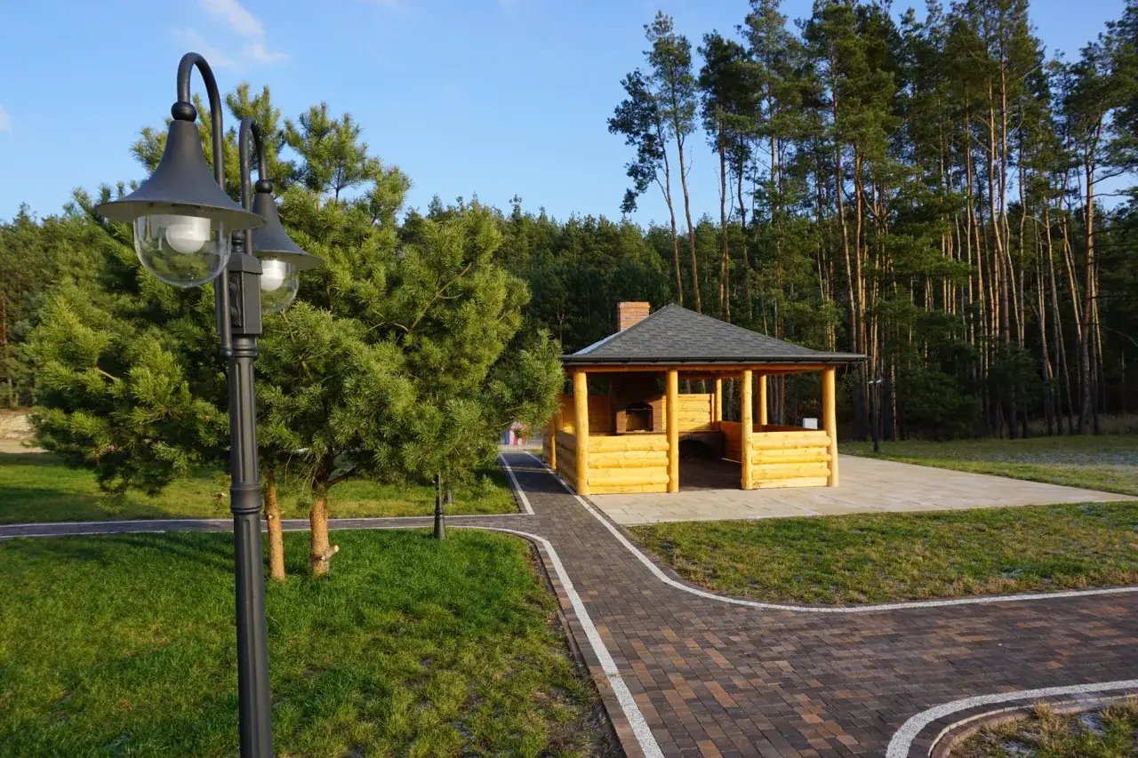 Drewniana altana z grillem i kominkiem, otoczona zielenią i lasem, idealne miejsce do wypoczynku w dom seniora Załęcze.