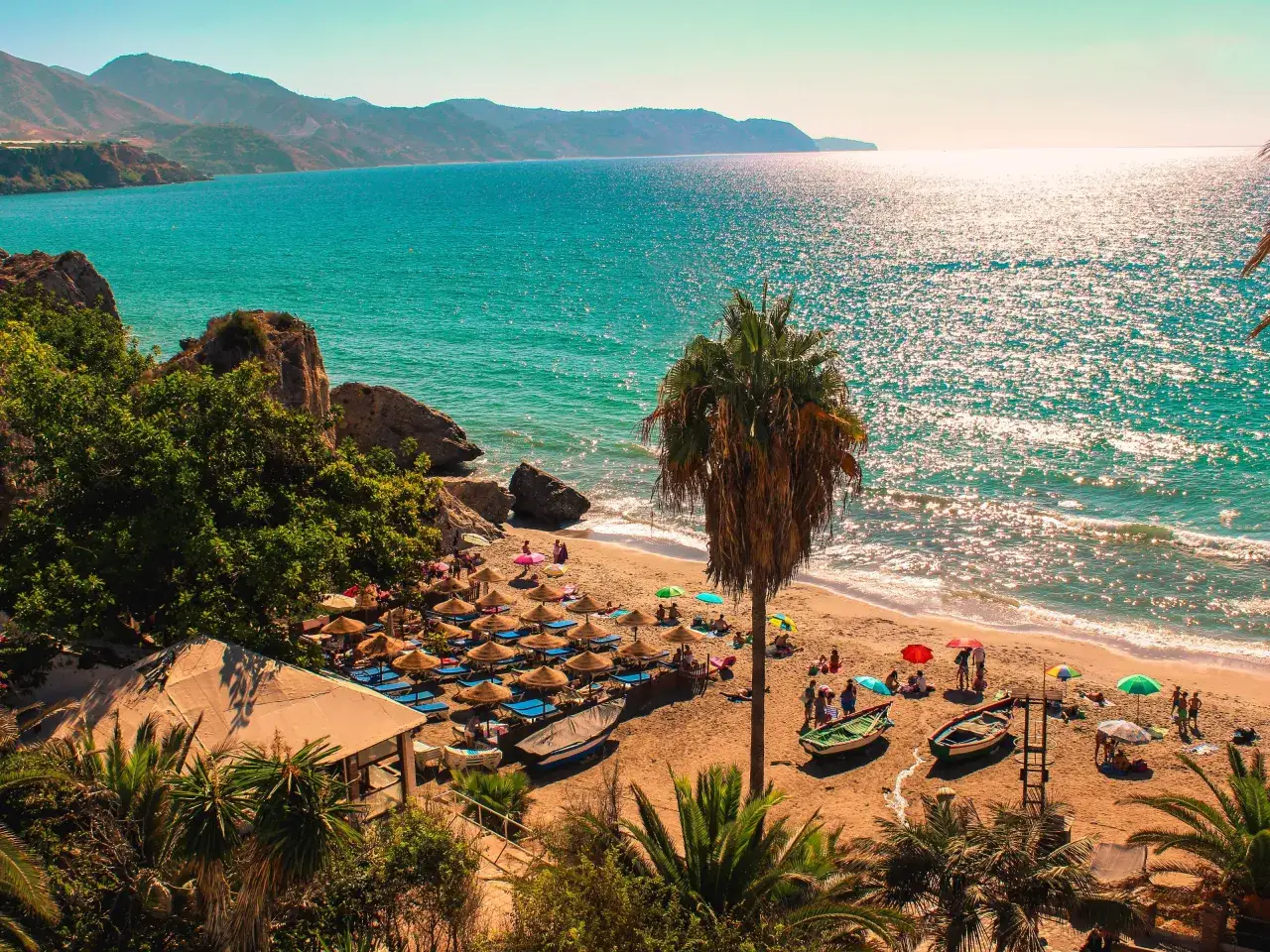 Malaga pogoda listopad: słoneczna plaża z palmami, leżakami i turkusowym morzem. Idealna pogoda na relaks.