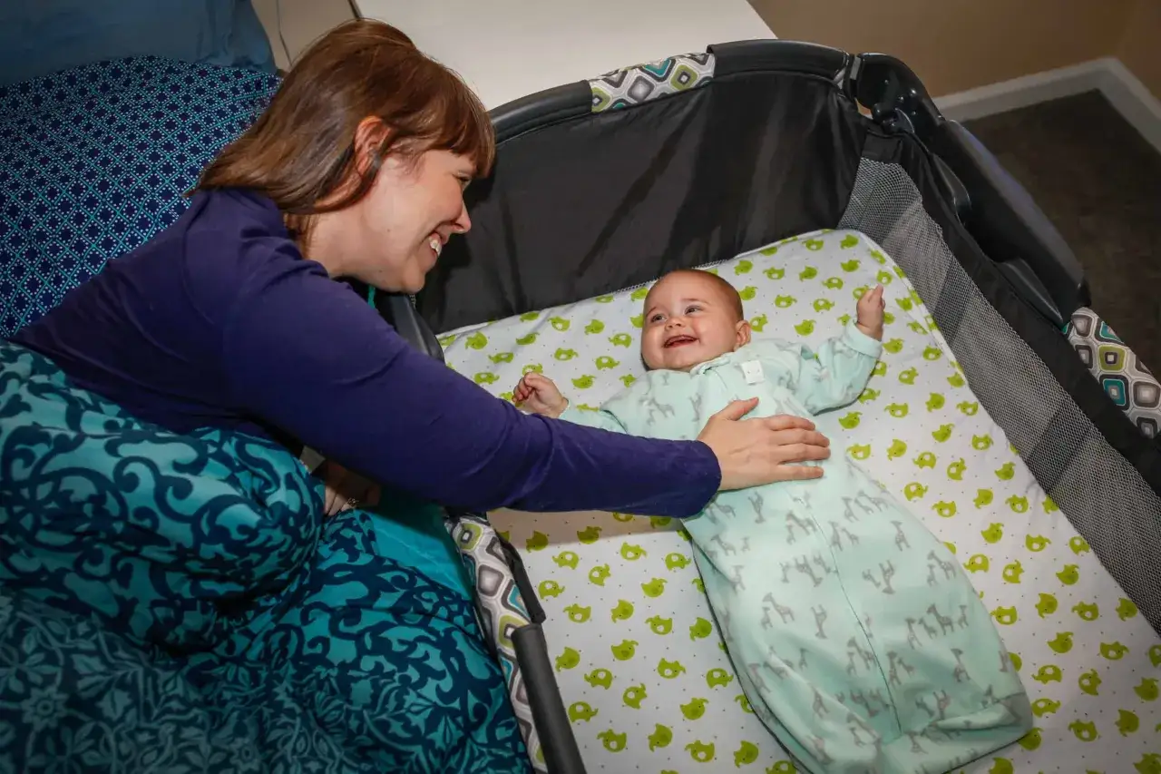 Madre sonr&iacute;e a su beb&eacute; en la cuna. Prevenci&oacute;n de muerte s&uacute;bita del beb&eacute;.