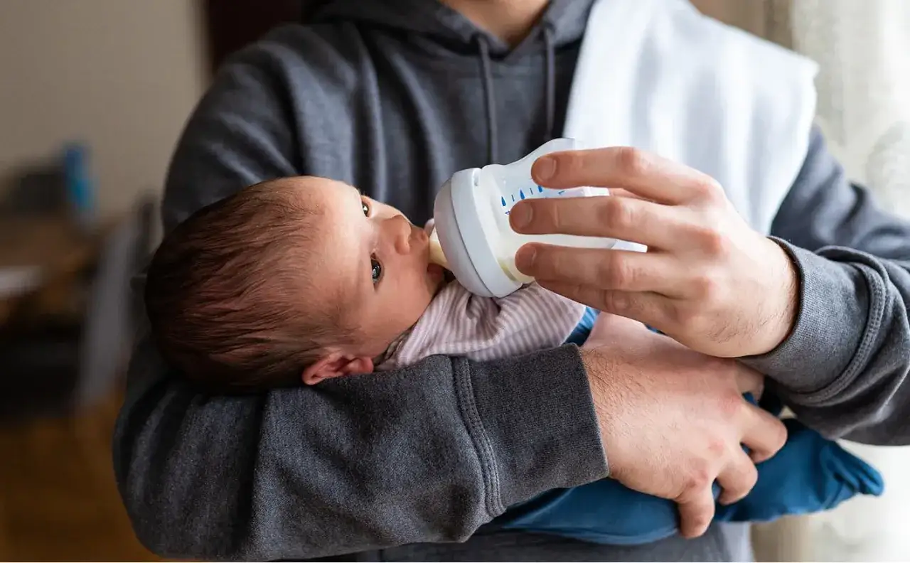 Un neonato mangia ogni 2 ore latte artificiale da un biberon tenuto da un uomo.