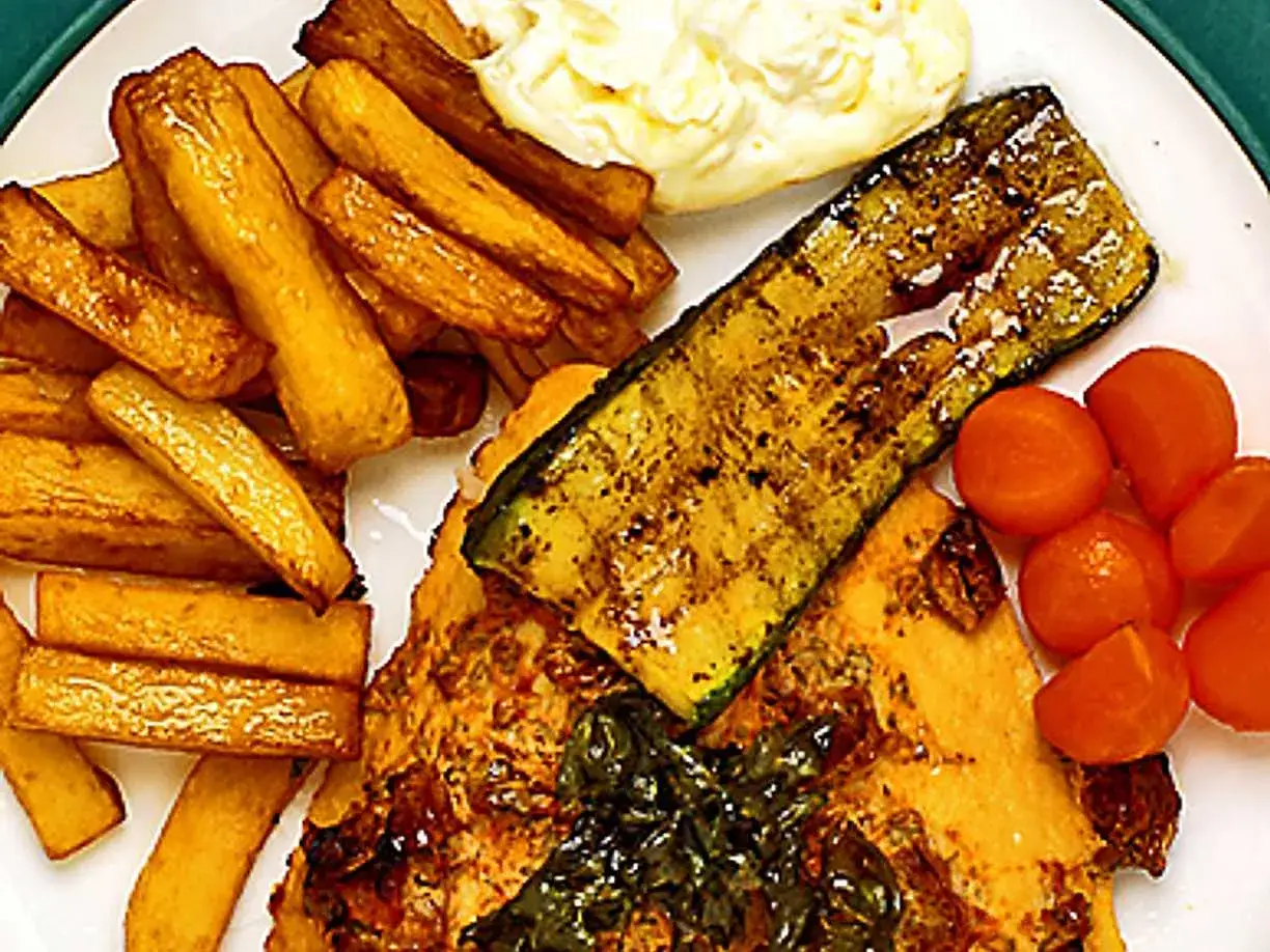En tallrik med gyllene pommes frites, grillad zucchini, körsbärstomater och en bit fisk. En härlig variant på fish and chips!