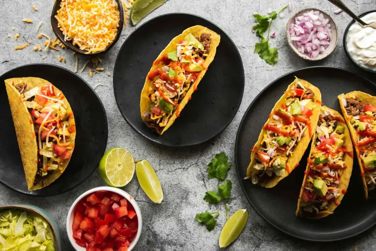 Leckere Taco-Rezepte: Tacos gef&uuml;llt mit Hackfleisch, K&auml;se, Avocado, Tomaten und Zwiebeln, garniert mit Koriander und Limettenspalten.