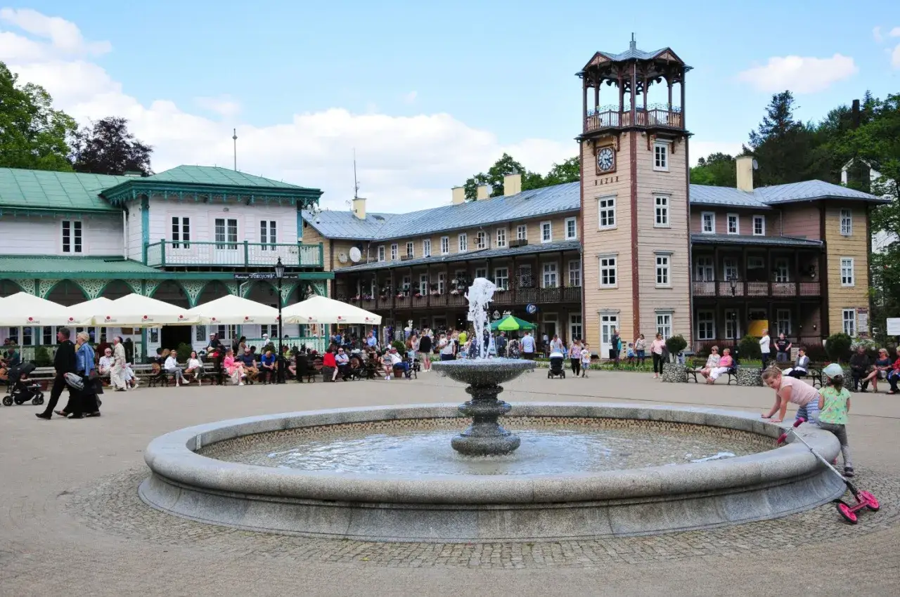 Iwonicz Zdrój atrakcje: Rynek z fontanną, zabytkowe budynki i spacerujący kuracjusze.