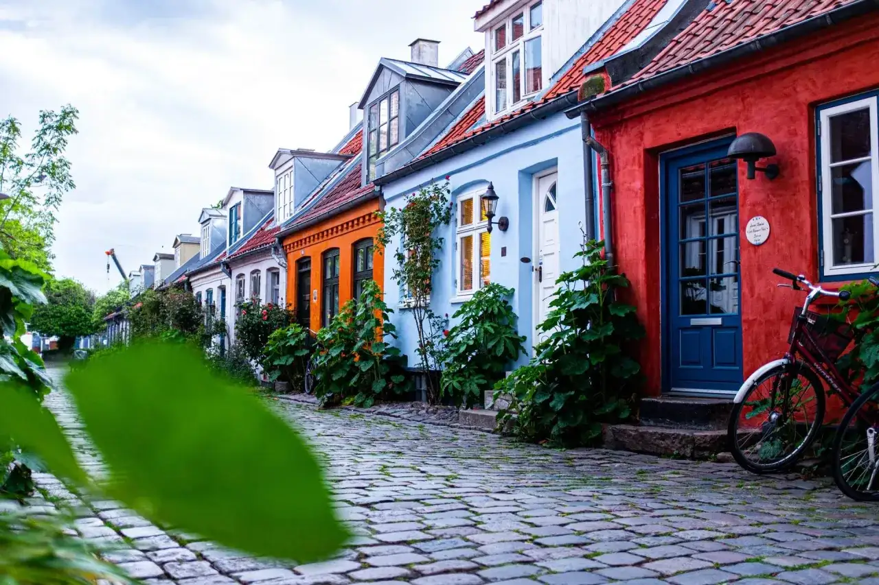 F&auml;rgglada hus l&auml;ngs en kullerstensgata, perfekt f&ouml;r en bilsemester i Danmark. En cykel st&aring;r parkerad vid ett r&ouml;tt hus med bl&aring; d&ouml;rr.