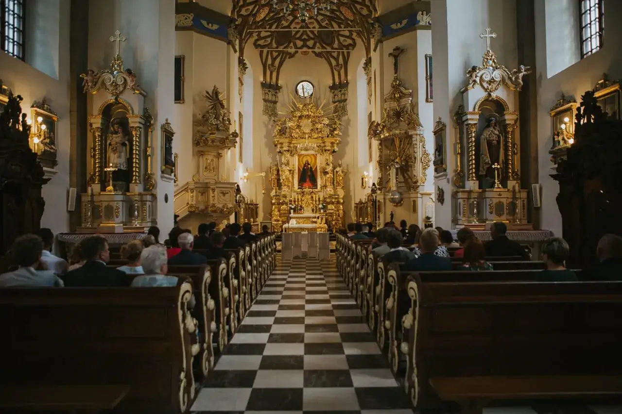 Wnętrze bogato zdobionej bazyliki w Polsce. Ludzie siedzą w ławkach, patrząc na ołtarz.