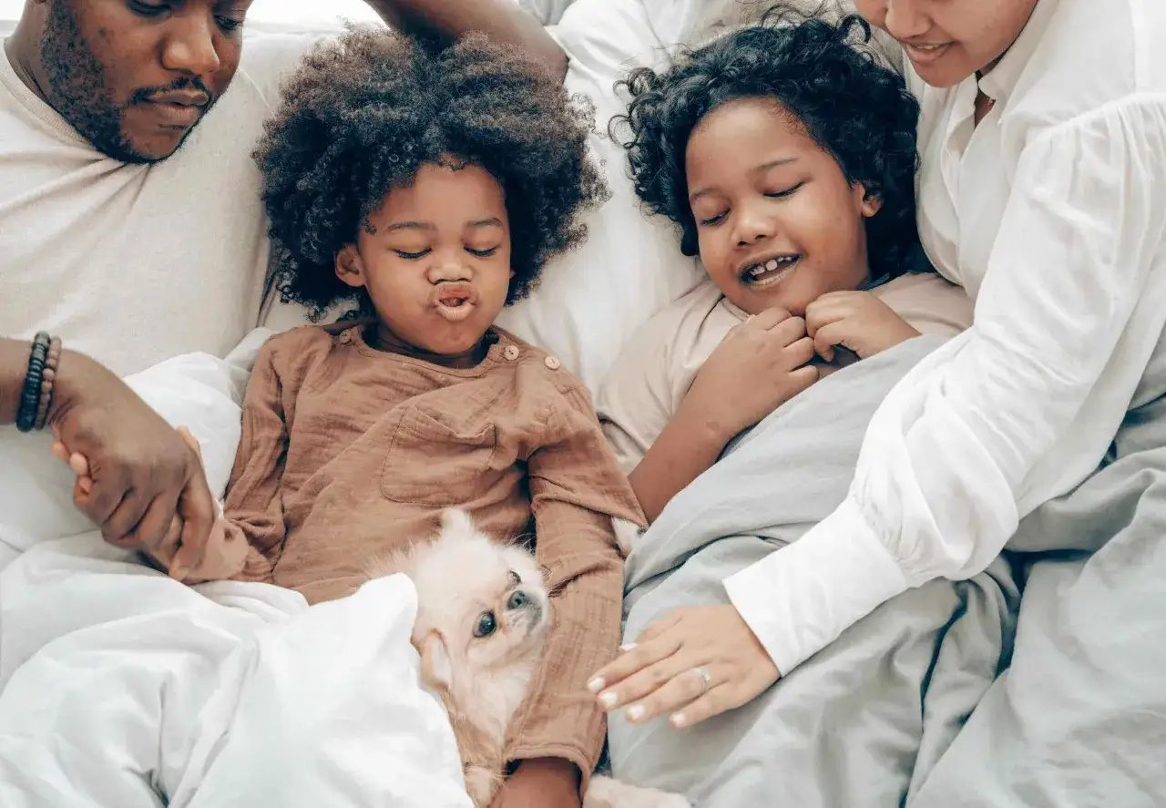 Familie kuschelt im Bett, um sich mit Kindern zu entspannen. Ein kleiner Hund liegt zwischen ihnen.