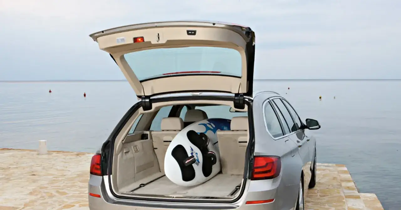 Srebrne bmw touring z otwartym bagażnikiem, w którym leży deska do windsurfingu, gotowe na wodne szaleństwo nad spokojnym morzem.