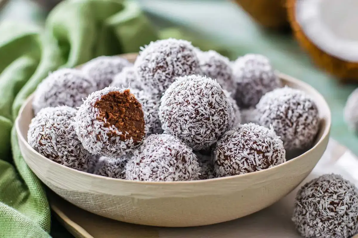 Una ciotola piena di dolcetti al cocco, uno &egrave; morso mostrando il ripieno al cioccolato.