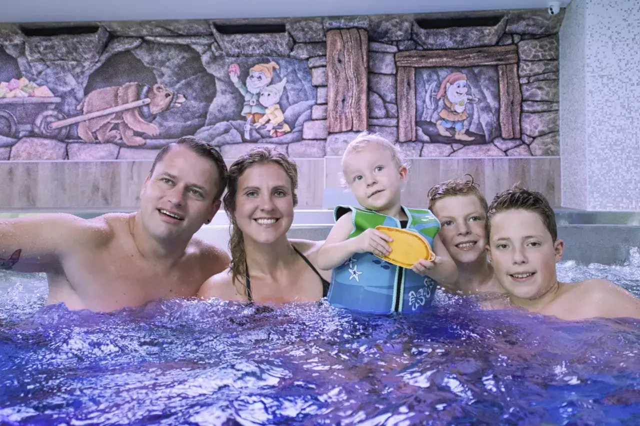 Familie im Pool mit Märchenfiguren an der Wand. Ein kleiner Junge trägt eine Schwimmweste, bereit für den TUI Kids Club Spaß.