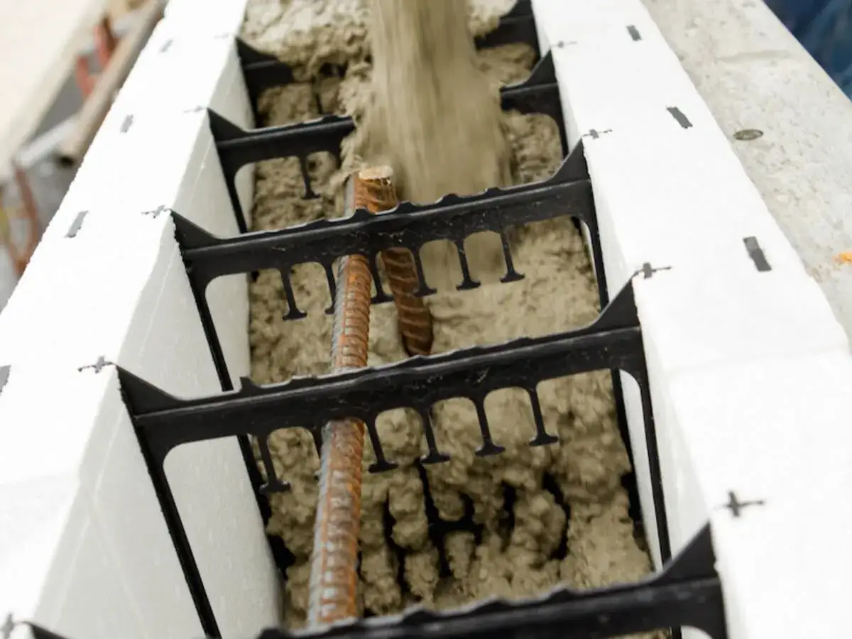 Beton flie&szlig;t in eine verlorene Schalung aus wei&szlig;en Schaumstoffelementen, die mit schwarzen Abstandhaltern und Bewehrungsst&auml;ben verbunden sind.