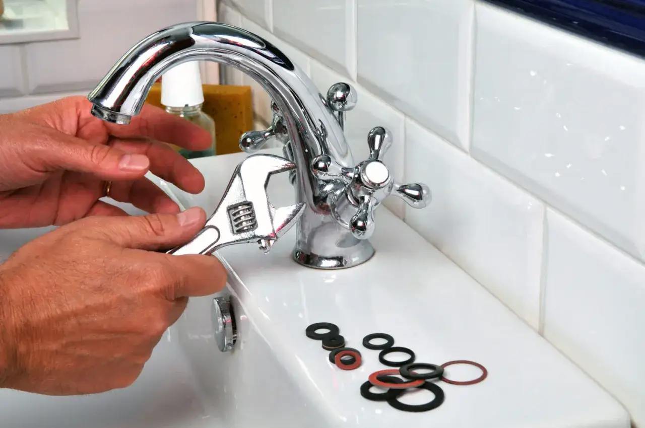 Main tenant utilise une clé pour changer un robinet. Des joints toriques sont posés sur le lavabo.