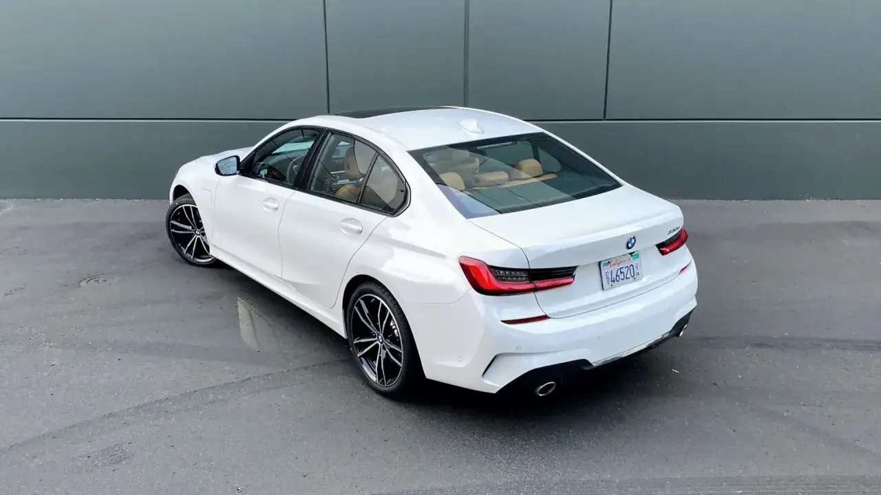 Białe BMW 330e z beżowym wnętrzem, zaparkowane przy szarej ścianie.