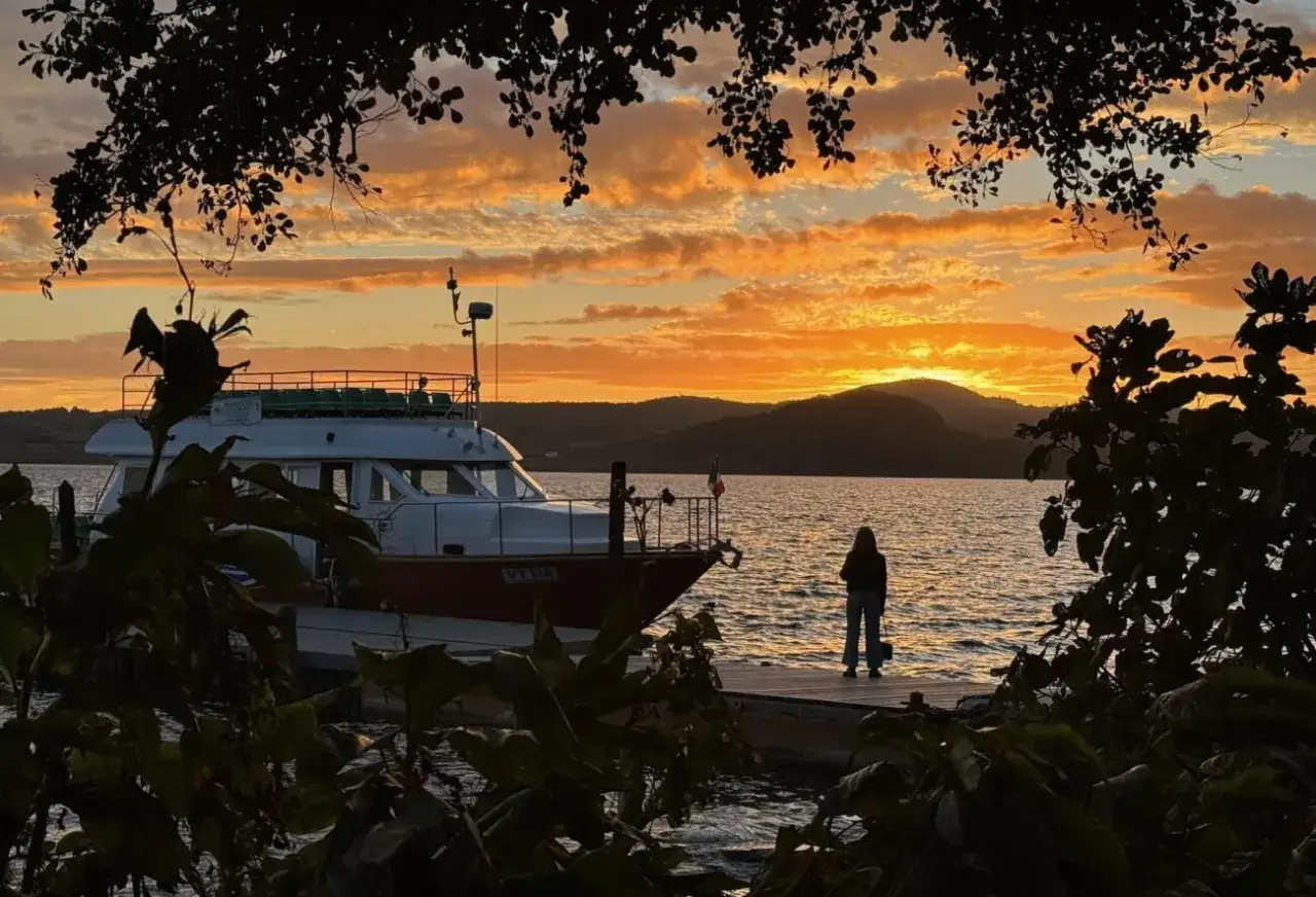 Tramonto infuocato sul lago, con una barca attraccata e una persona che ammira il panorama. Un'indimenticabile visita all'isola Martana.