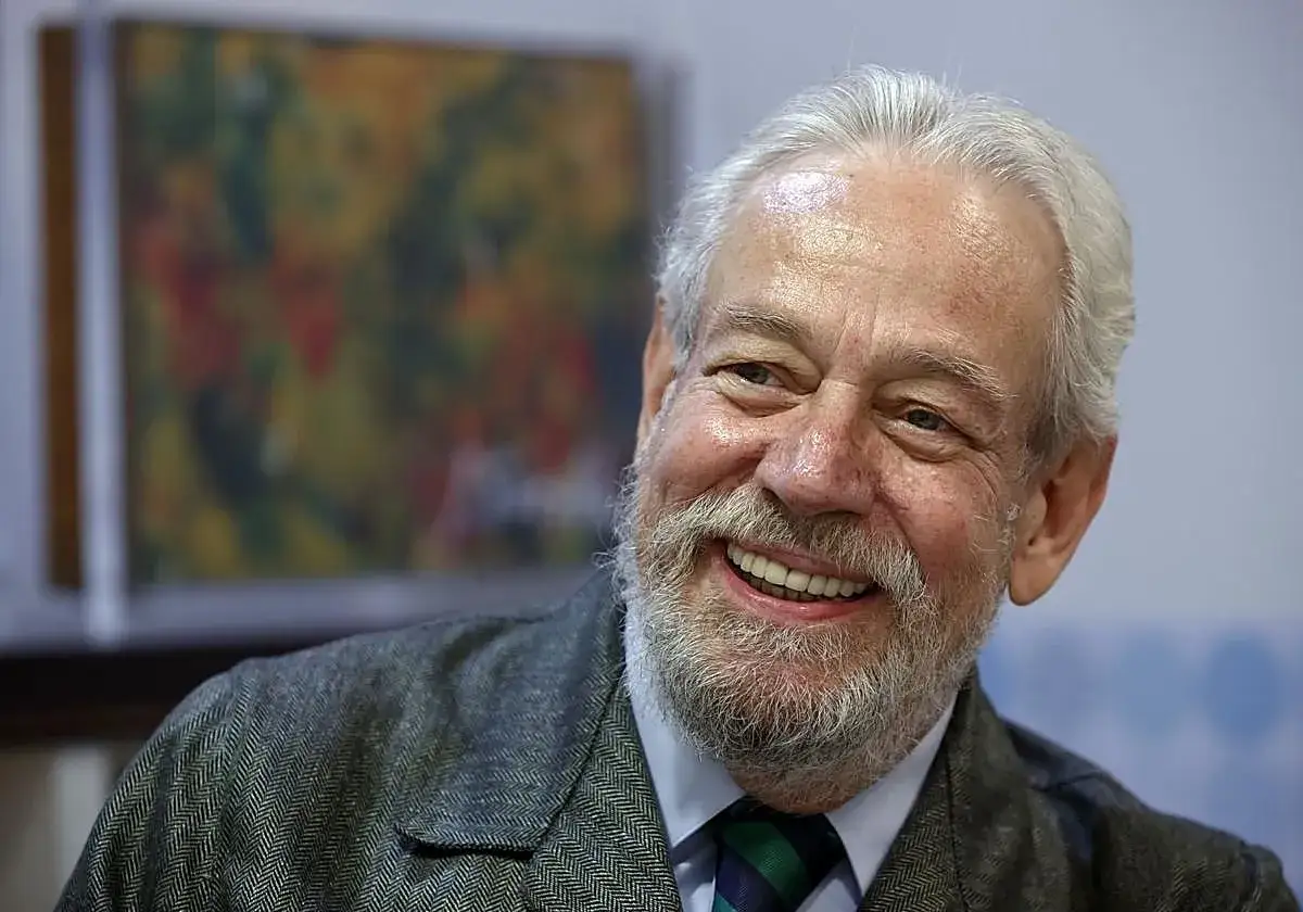 Retrato de Carlos Blanco Aguinaga, un hombre mayor con barba canosa y una sonrisa radiante, vestido con traje y corbata.