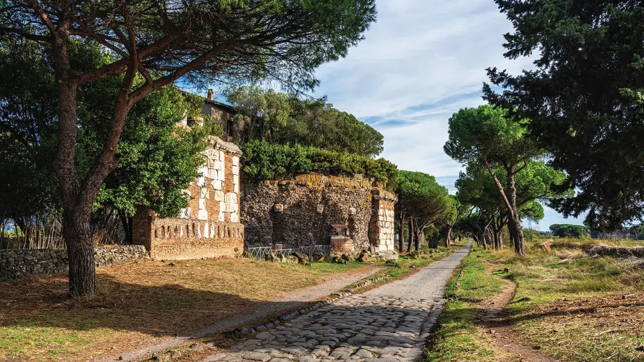 Kamienna droga Via Appia, otoczona drzewami i starożytnymi ruinami, zaprasza do podróży w czasie.