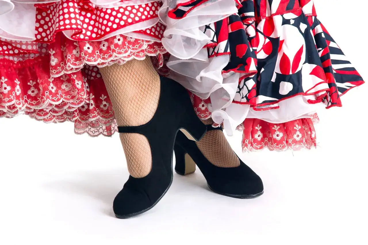 Pies con zapatos negros y medias de rejilla, listos para el zapateo flamenco entre volantes de lunares y flores.
