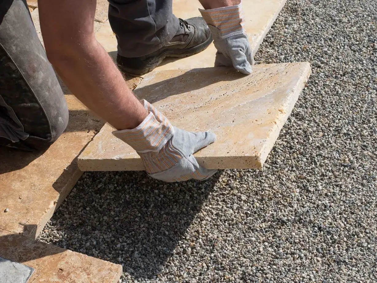 Arbeiter verlegt Steinplatten f&uuml;r eine Splitt-Terrasse.